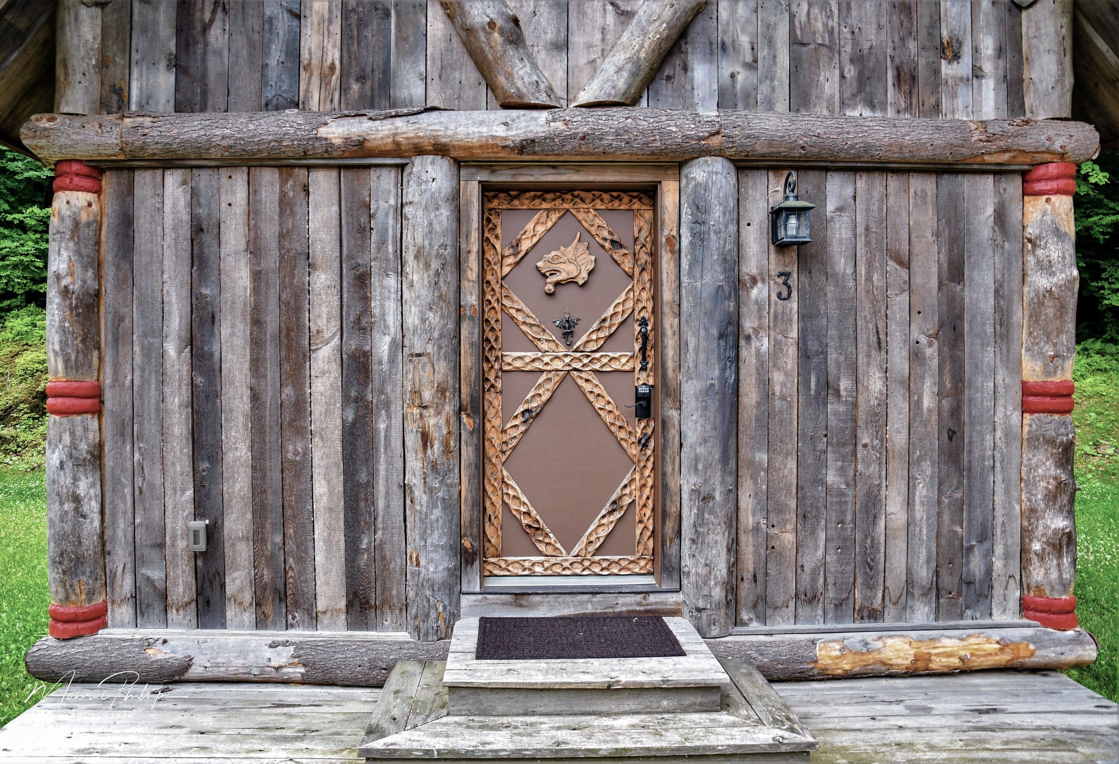 A rustic wooden cabin with a decorative door featuring a geometric pattern and a wolf head emblem.