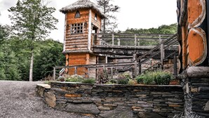 A rustic wooden cabin with a thatched roof, a stone wall, and a wooden staircase leading to a balcony. - Vikings Villages Resort (Guilford)
