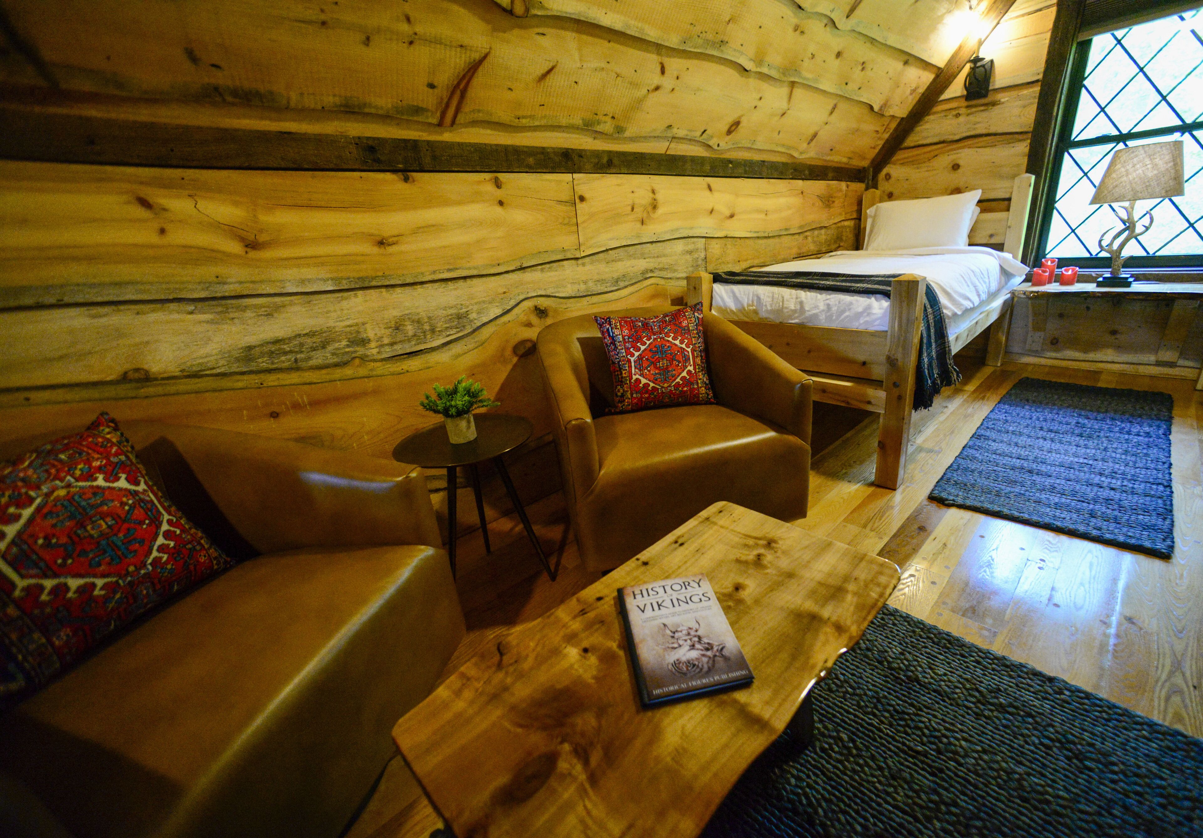 Acogedora habitación de cabaña de madera con una cama, dos sofás de cuero, una mesita y un ventanal con vistas.