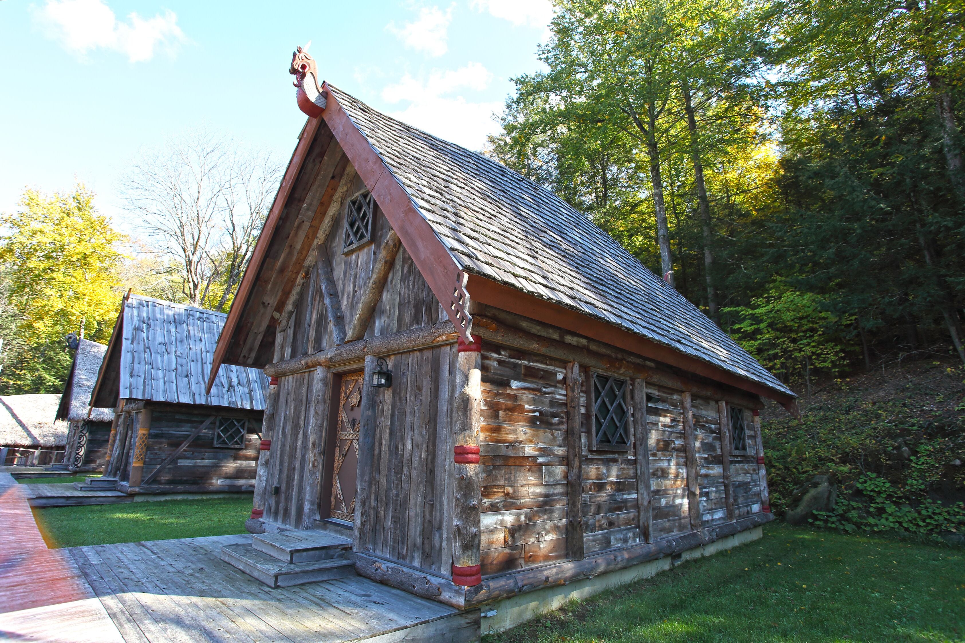 A rustic log cabin with a steeply pitched roof, a wooden porch, and a small front yard.