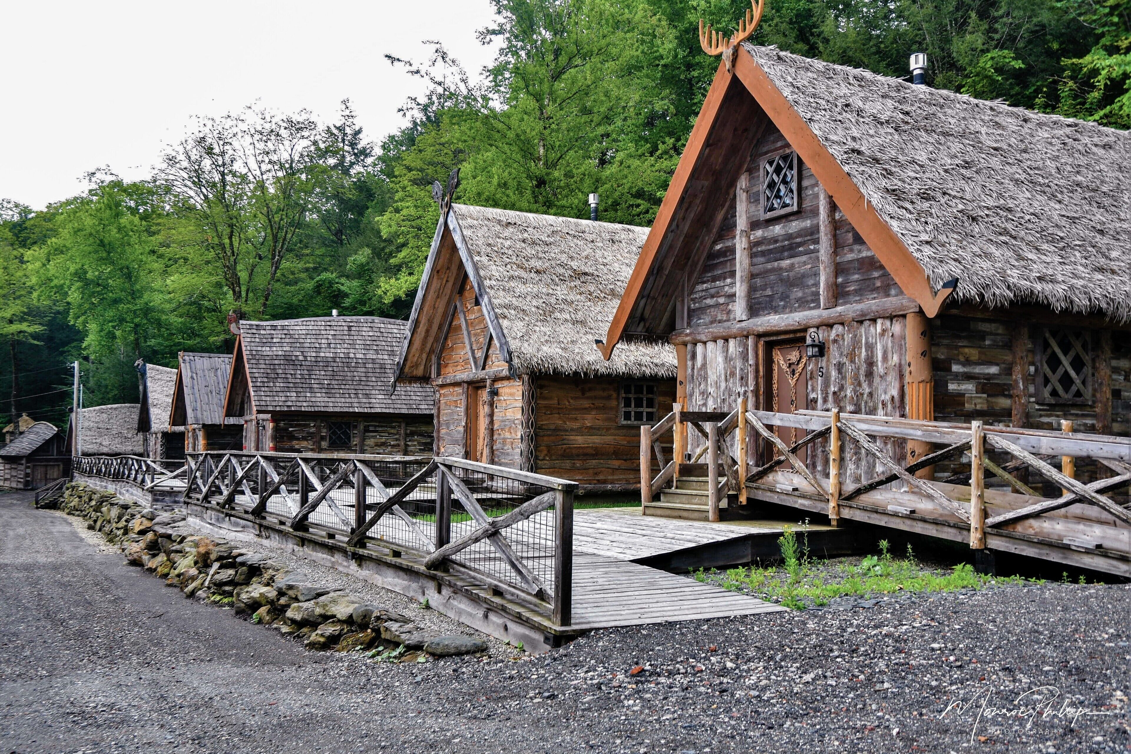 Une cabane rustique en bois, dotée d’un toit de chaume, d’une terrasse en bois et d’un mur en pierre.