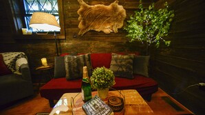 A cozy room with a wooden wall, a red sofa, a small table with a bottle, a book, and a plant. - Vikings Villages Resort (Guilford)