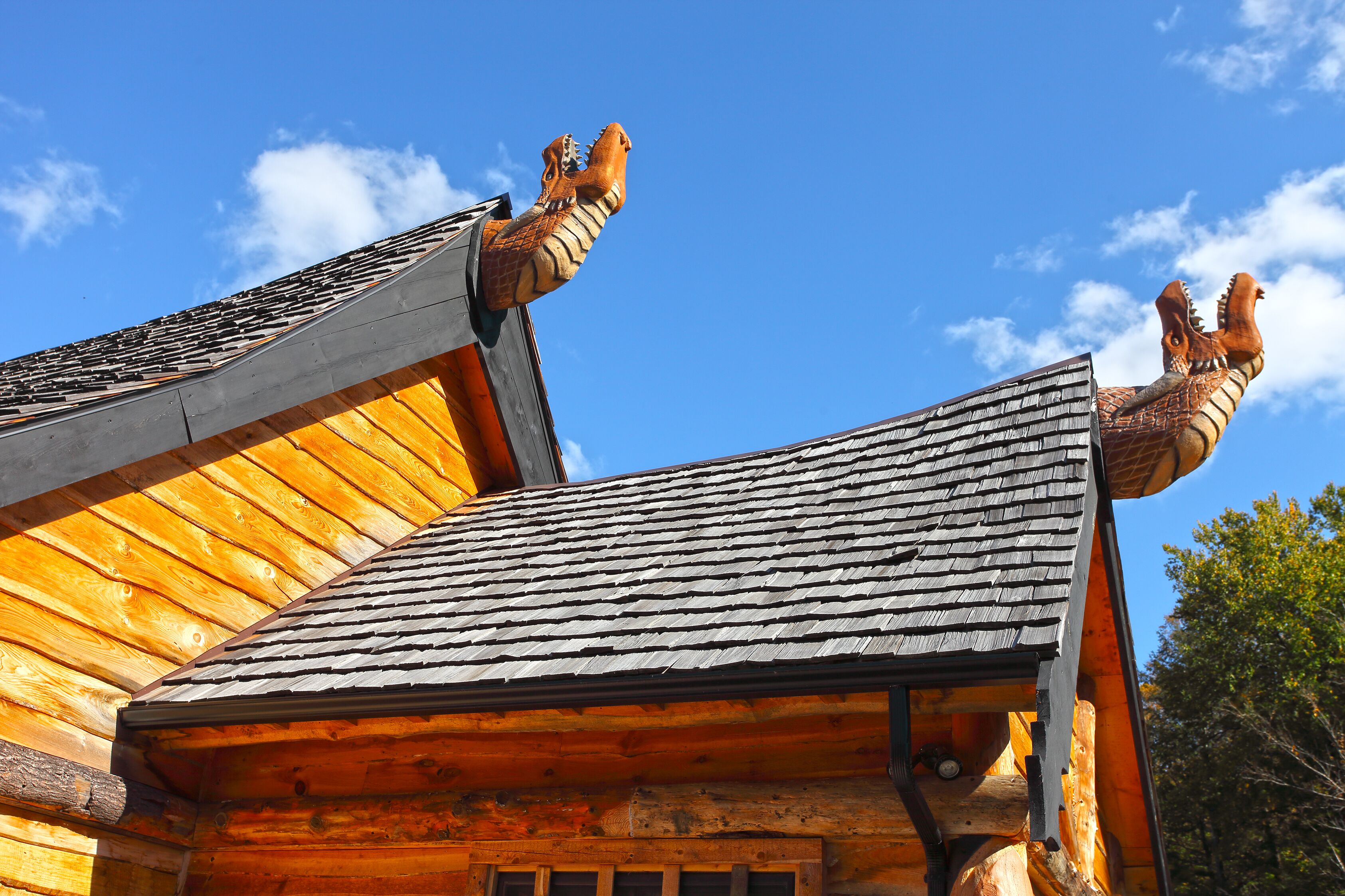 Een houten chalet met een schuin dak en twee grote, gebeeldhouwde dierenkoppen op de dakrand.