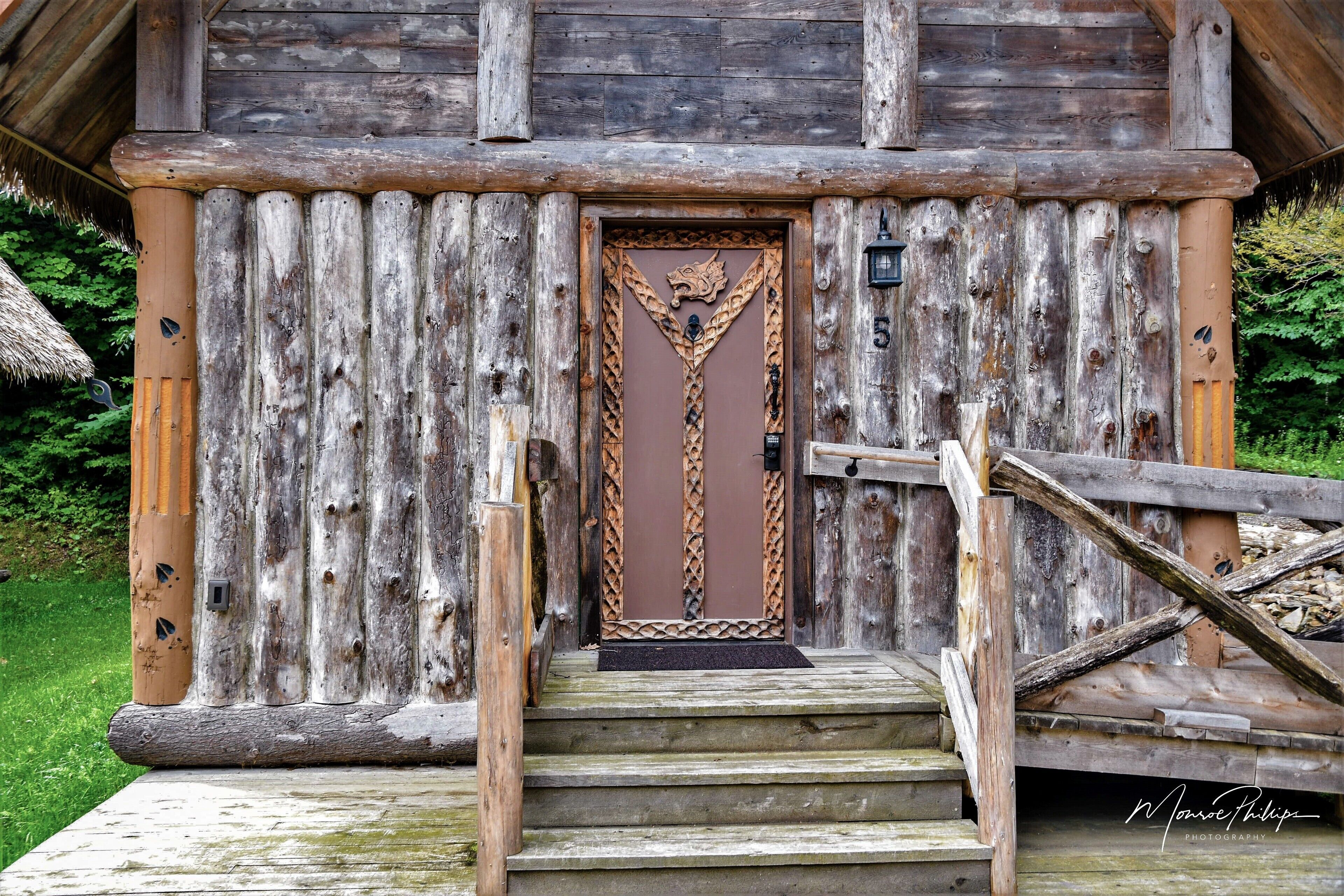 A rustic wooden cabin with a decorative door, a staircase leading to the entrance, and a wooden fence.
