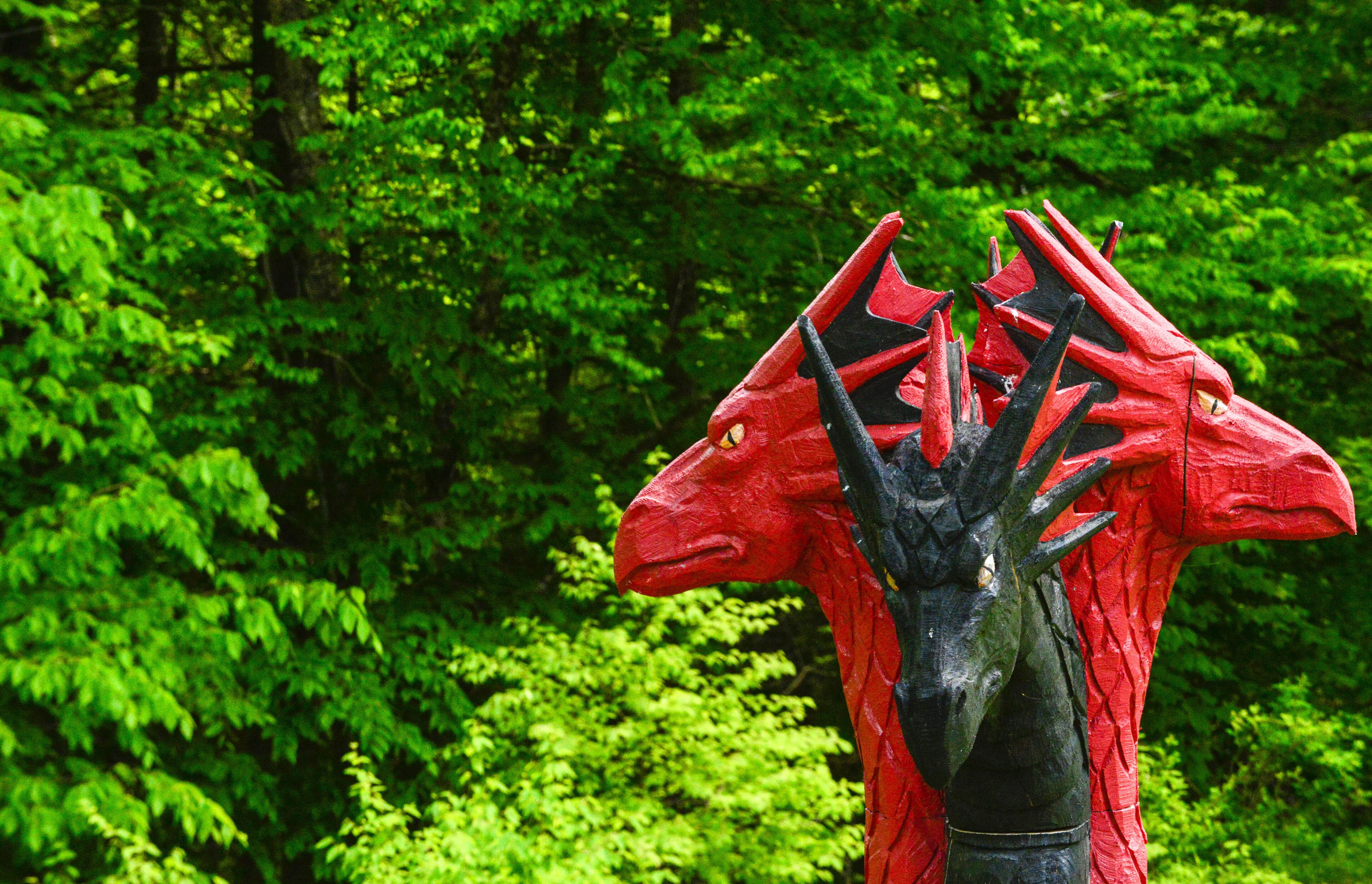 A red sculpture of a mythical creature in a forest.