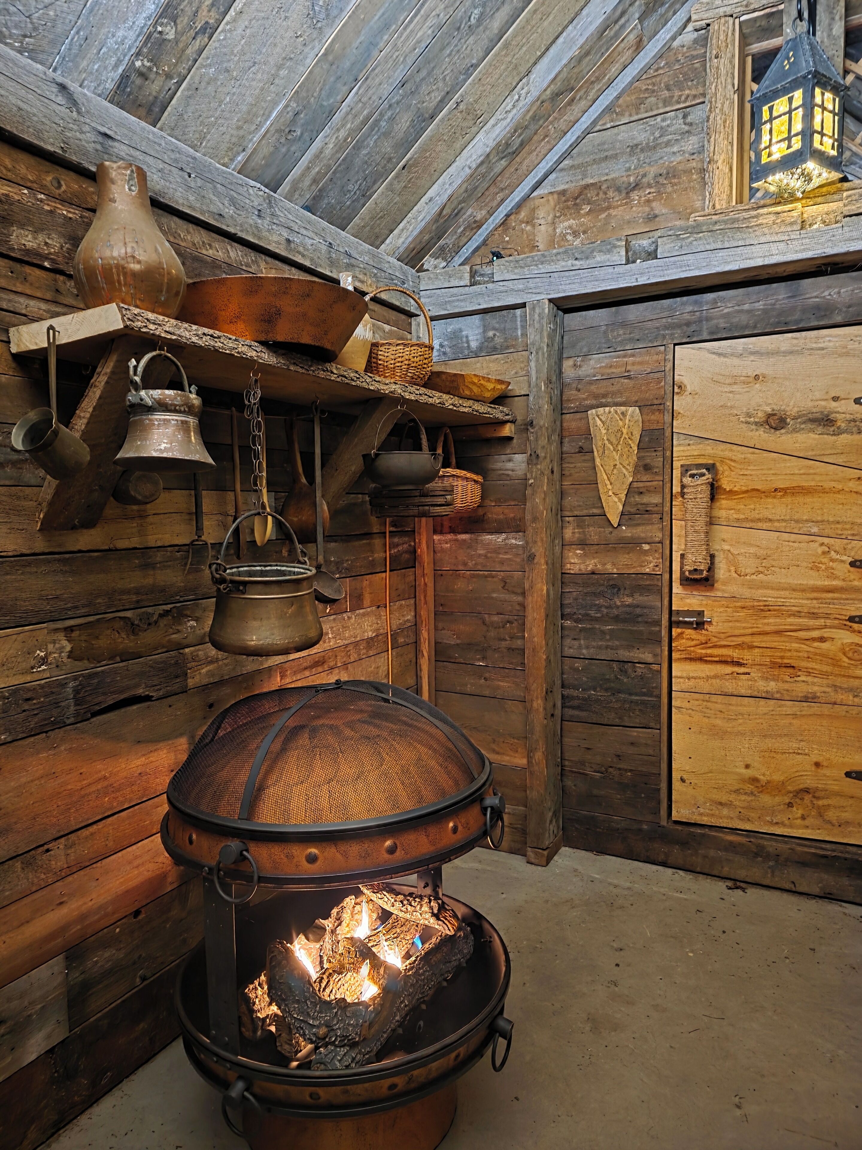 A rustic wooden interior with a large metal stove, wooden shelves with various items, and a wooden door.