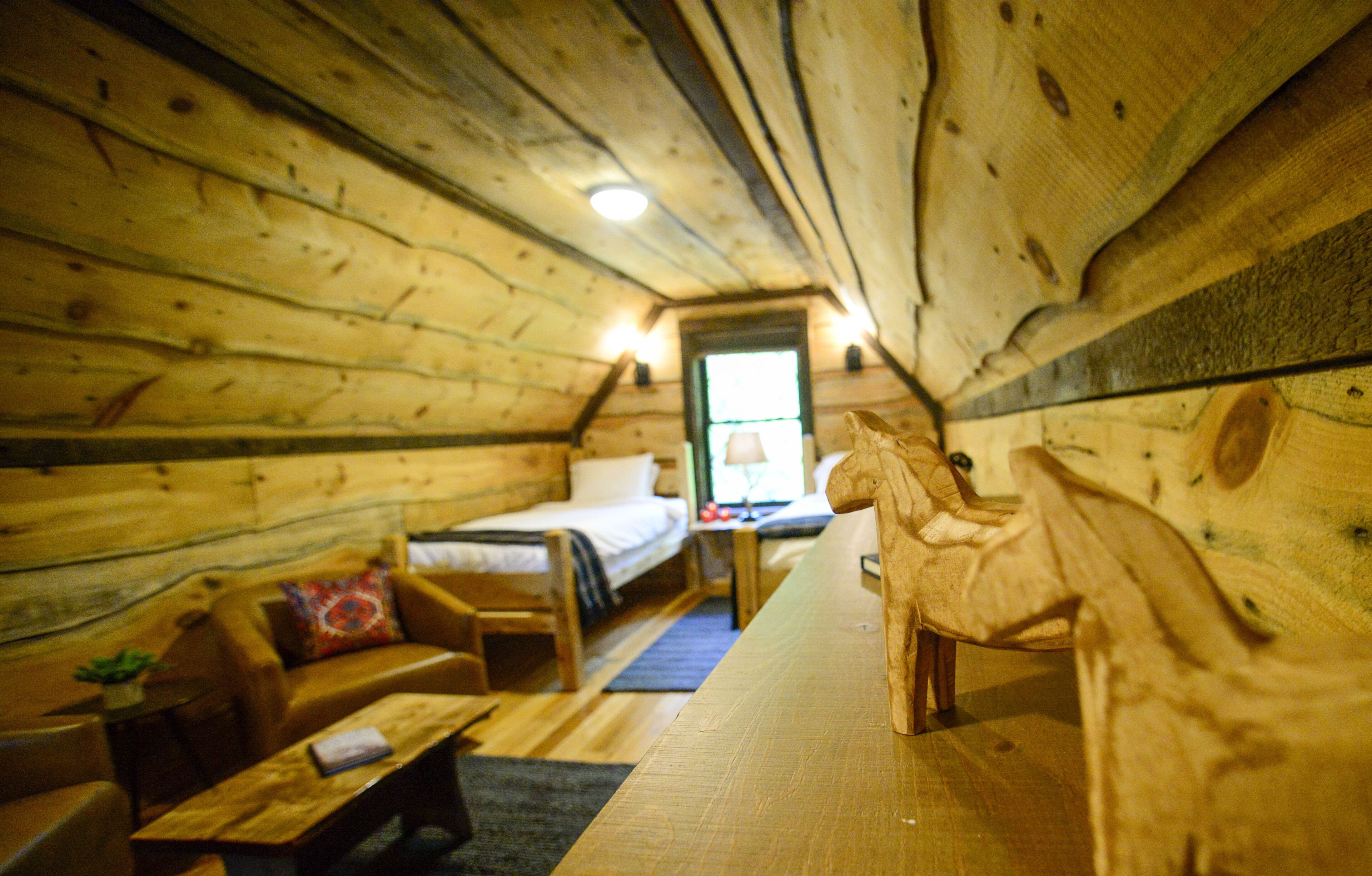 A cozy cabin interior with wooden walls, a bed, a sofa, and a dining table.