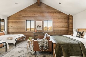 A bedroom with two beds, a wooden sloped ceiling, a small table, and a chair.