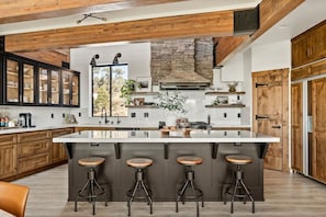 A modern kitchen with a large island, wooden cabinets, and a stone fireplace.