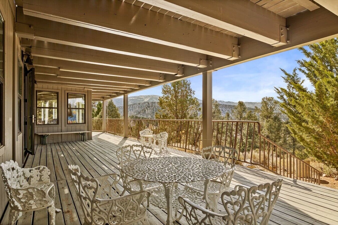 A covered outdoor deck with a table and chairs, overlooking a mountainous landscape.