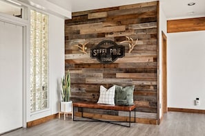 A room with a wooden wall, a bench, a potted plant, and a sign reading 'STEEL PINE LODGE'. - Steel Pine Lodge · Steel Pine Lodge A Rustic Mountain Retreat Views! (Big Bear)