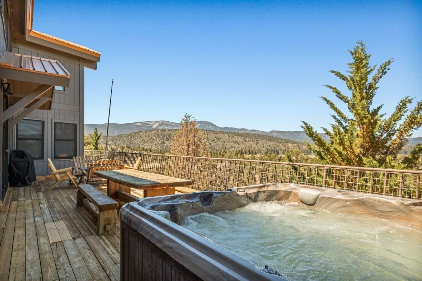 A wooden deck with a hot tub, outdoor furniture, and a view of mountains.