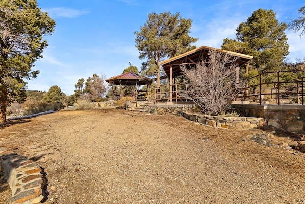 A rustic outdoor area with a wooden gazebo, stone steps, and a gravel ground.