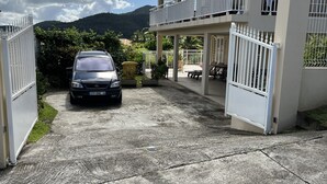Een omheind landgoed met een auto ervoor, een overdekt terras en een bergachtige achtergrond.
