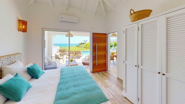 Una camera da letto con un letto, vista mare e una porta scorrevole che dà su un'area esterna con sedie e un tavolo.