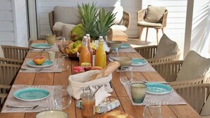 Un tavolo da pranzo in legno apparecchiato con piatti, bicchieri, una pagnotta e diversi tipi di frutta e bevande.