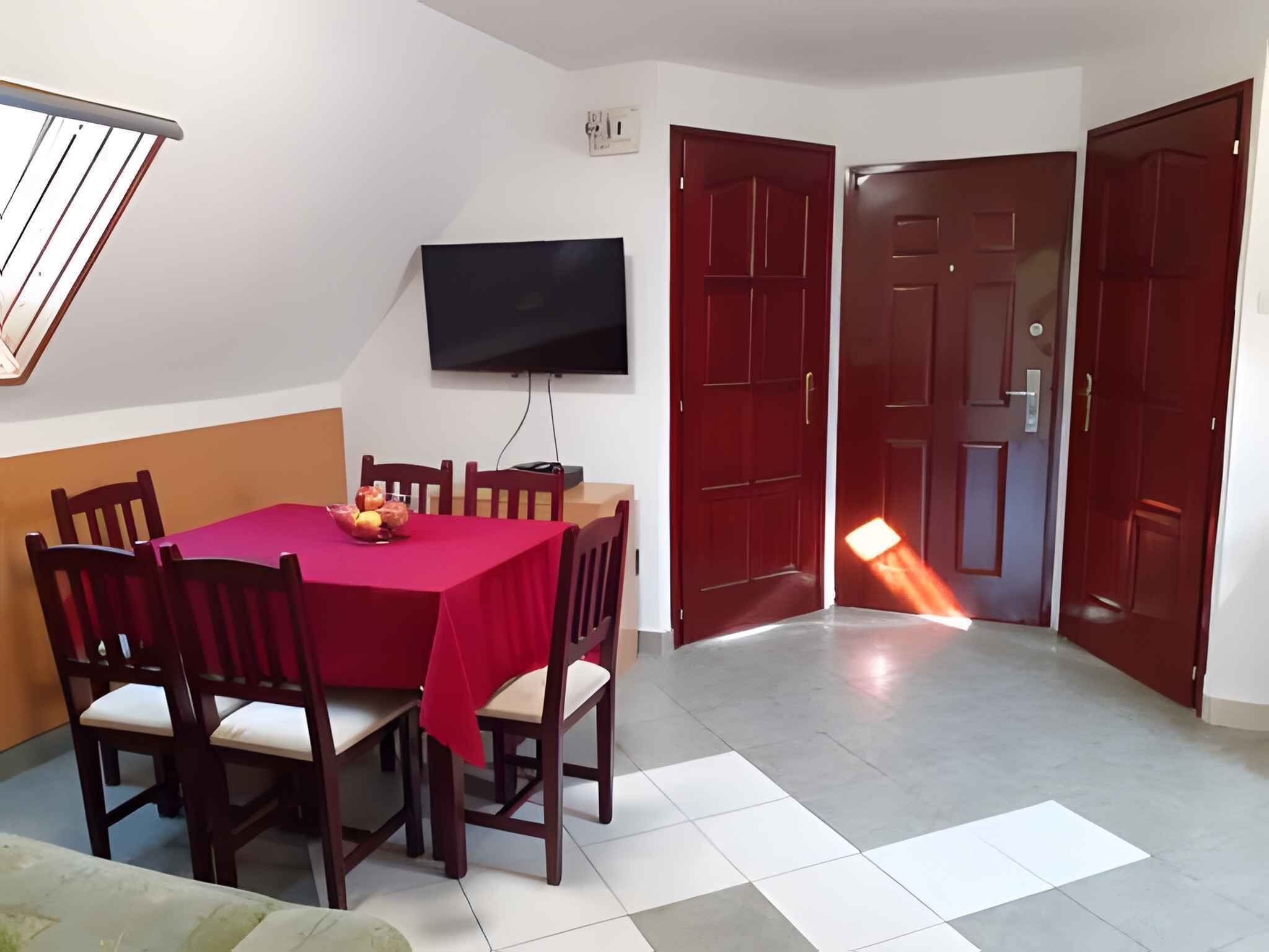 Un comedor con una mesa y sillas rojas, un televisor de pantalla plana montado en la pared y dos puertas rojas.