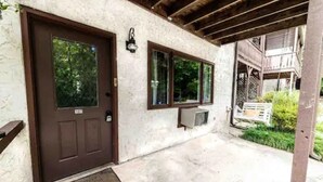 A building entrance with a brown door, a window, and a small outdoor area with a bench and greenery. - Paul's Apartment - 55in TV, Wi-Fi, kitchenette (Helen)