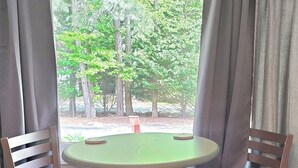 A room with a round table, two chairs, a window with curtains, and a view of trees. - Paul's Apartment - 55in TV, Wi-Fi, kitchenette (Helen)