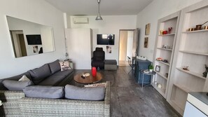 En moderne stue med sofa, sofabord og fjernsyn. Der er et bogskab og et spiseområde med bord og stole.