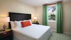 Una habitación de hotel con una cama grande, dos mesitas de noche con lámparas, cortinas verdes y una ventana con vista a palmeras.
