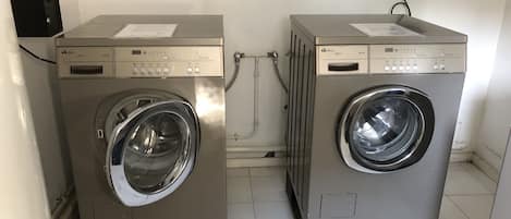 Two front-loading washing machines in a room with white tiled floors and a plain wall.