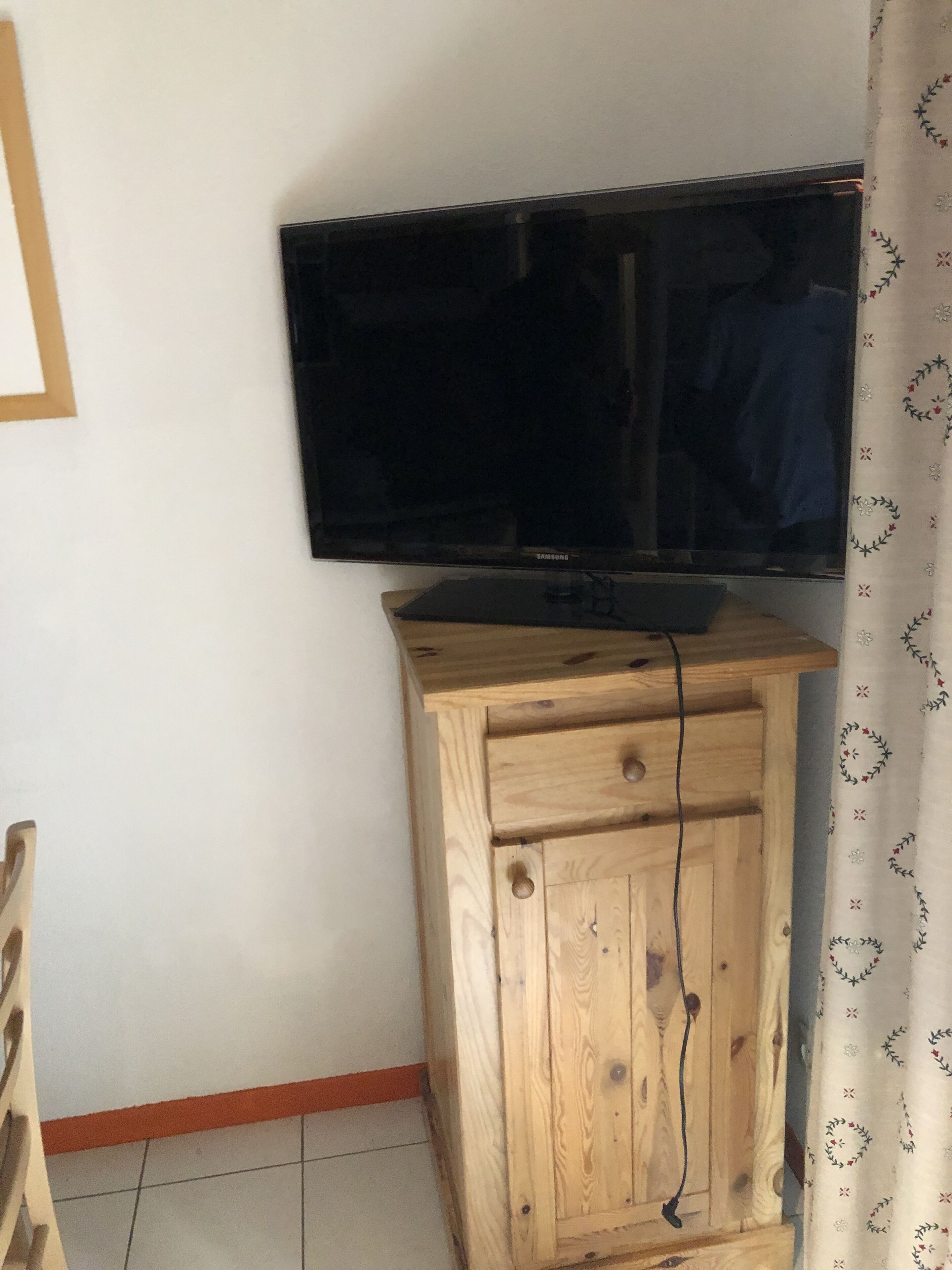 Un mueble de madera con un televisor de pantalla plana encima, una cortina con estampado floral y un suelo de baldosas.