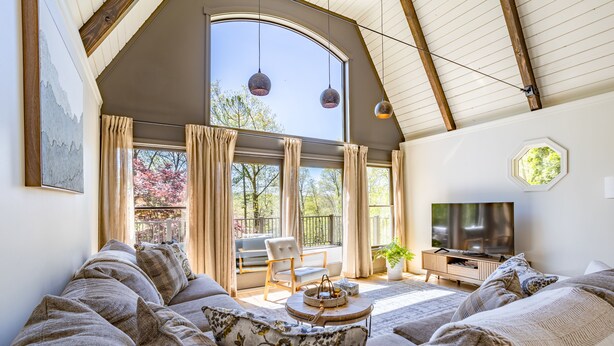 Een ruime woonkamer met een grote zithoek, een televisie en een balkon met gordijnen.
