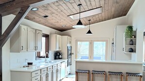 Een ruime keuken met houten balken, witte kasten en een groot eiland met barstoelen.