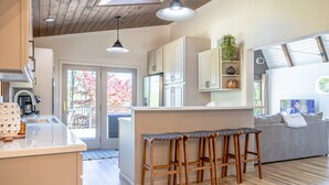Een moderne keuken met houten kasten, een centraal eiland met krukken en een zithoek met een grijze bank.