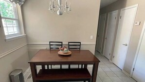 A dining room with a wooden table, chairs, a chandelier, and a trash can. - The hunt club (Tulsa)