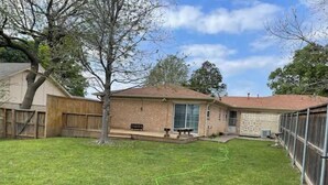 A backyard with a grassy lawn, a wooden fence, a brick house, and a tree. - The hunt club (Tulsa)
