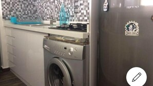 A kitchen with a washing machine, a tiled backsplash, and a refrigerator with a sticker.