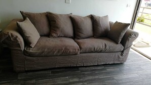 A brown sofa with multiple cushions in a room with dark wooden flooring and a large window.
