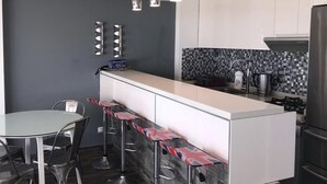 A modern kitchen with a central island, bar stools, a dining table, and stainless steel appliances.
