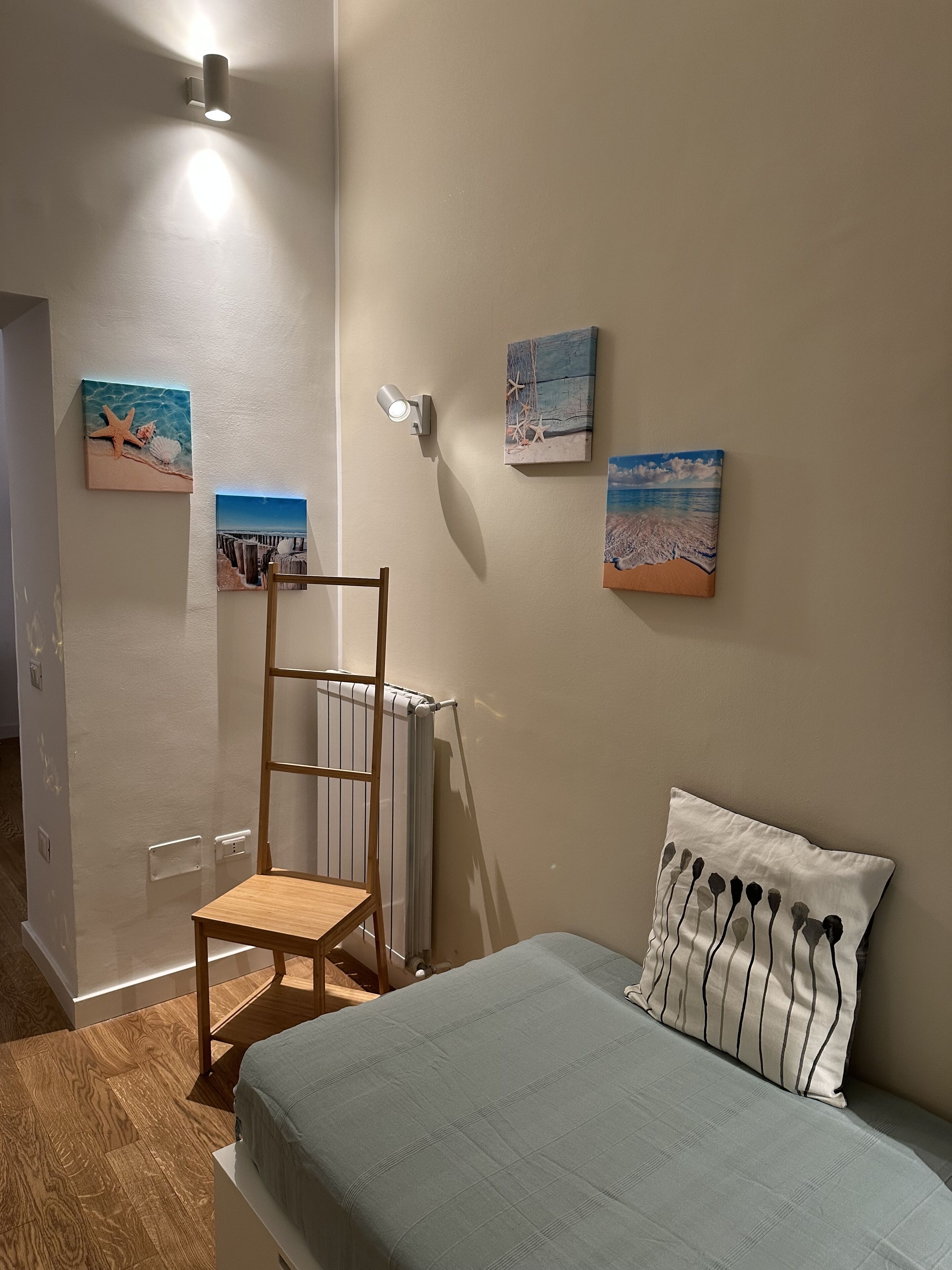 A bedroom with a bed, a chair, a radiator, and wall art.