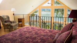 Une chambre à coucher avec un grand lit, une chaise, une table de chevet et une fenêtre donnant sur une étendue d’eau.