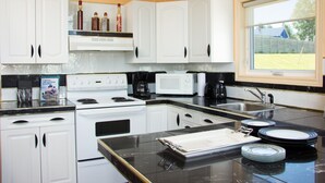 Une cuisine avec des meubles blancs, une cuisinière, un four à micro-ondes et un évier.
