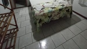 Ein Schlafzimmer mit einem Bett, einem Holzstuhl, einem kleinen Bild an der Wand und einem Fenster mit Vorhängen.