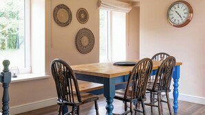 Een eethoek met een houten tafel, vier stoelen, een wandklok en geweven wanddecoratie.