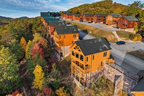 A lodge with multiple wooden cabins, a paved driveway, and a backdrop of autumn-colored trees. - Epic Mountain Views, Hot Tub, Sleeps 10, Pool Table, Arcade, Foosball, Fast WiFi (Sevierville)