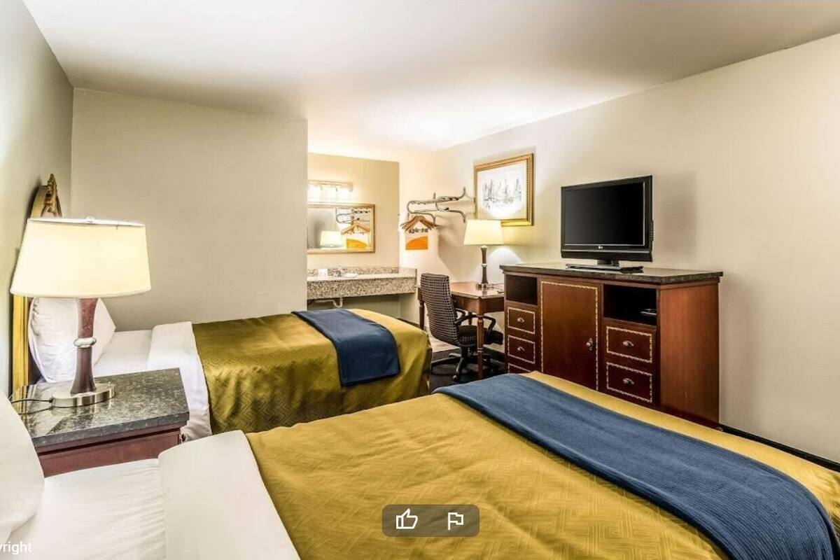 A hotel room with two beds, a desk, a television, and a cabinet.