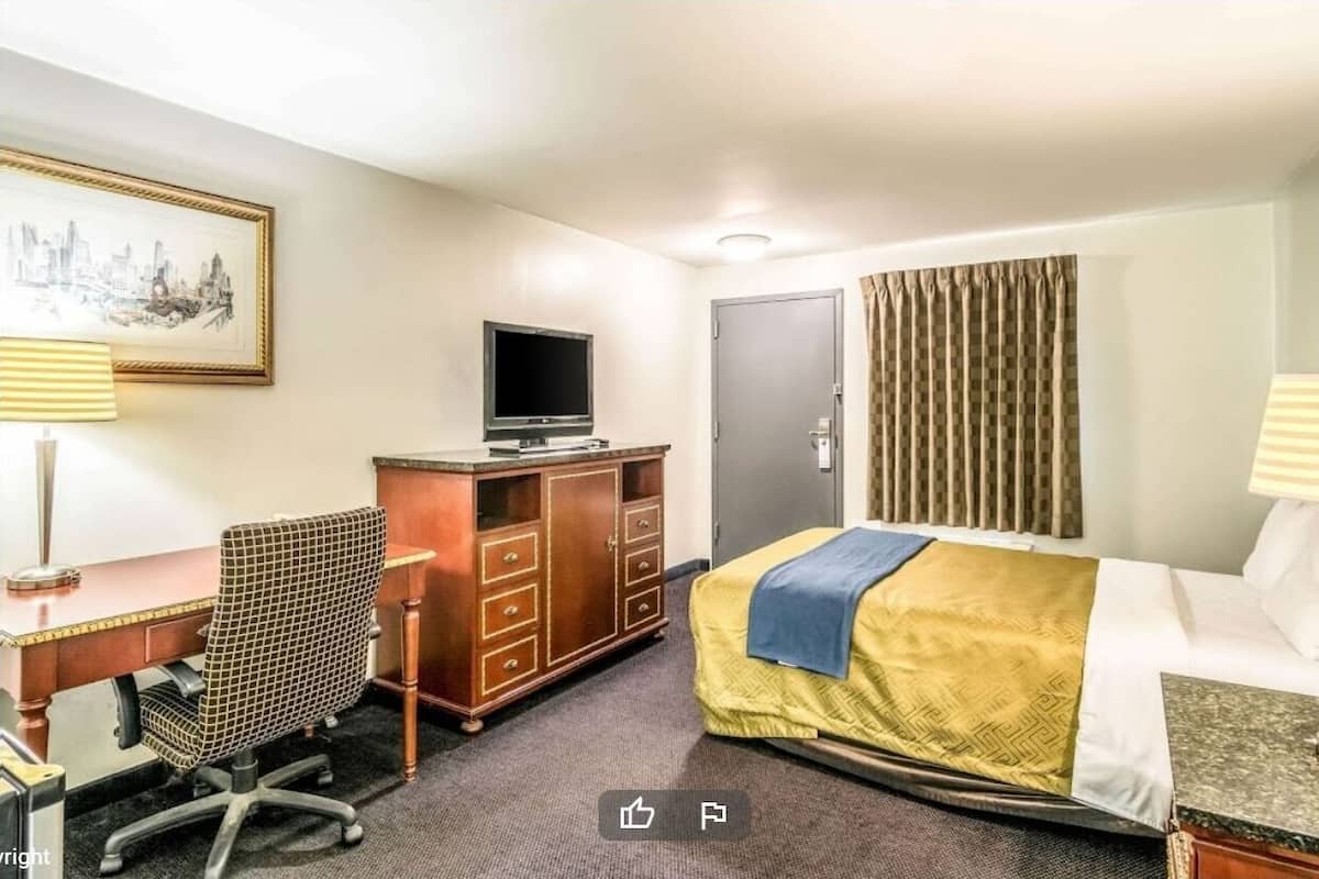 A hotel room with a bed, a desk with a chair, a television, a wardrobe, and a door.
