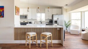A modern kitchen with white cabinets, a central island with stools, and pendant lighting.