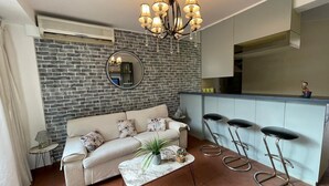 Een woonkamer met een bank, salontafel en een keukenhoek met een barkruk.