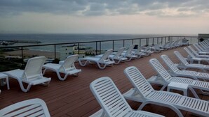 Een terras met witte lounge stoelen gericht op de oceaan, een leuning en uitzicht op het strand en de zee.