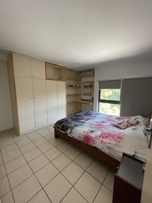 A bedroom with a bed, a wardrobe, a small table, and a window. - Duplex at Siwar Resort, 1 bedroom, Wi-Fi, parking, near Rimal (ZOUK MOSBEH)