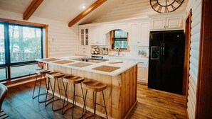 Una cocina con una isla grande, taburetes de madera, un refrigerador negro y un reloj en la pared.