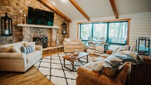 Una sala de estar acogedora con chimenea de piedra, vigas de madera y ventanas amplias.