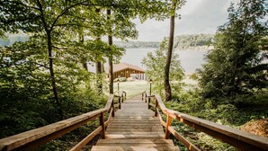 Una escalera de madera lleva a un albergue junto al lago, rodeado de árboles.